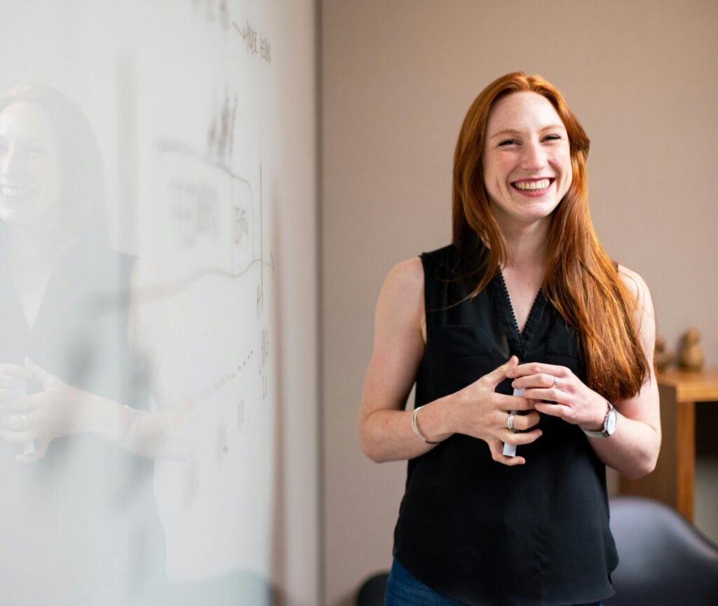 Red haired girl smiling while presenting next to a whiteboard